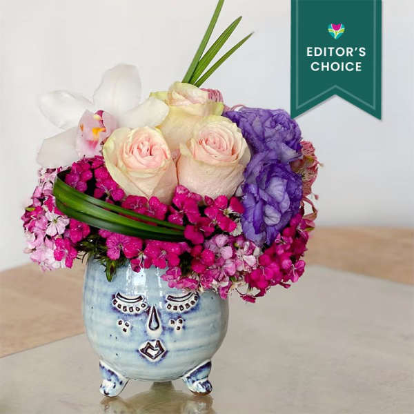 Pink and white roses with purple flowers in a face-shaped ceramic vase