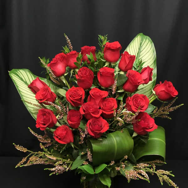 Bouquet of red roses with broad green leaves in a glass vase