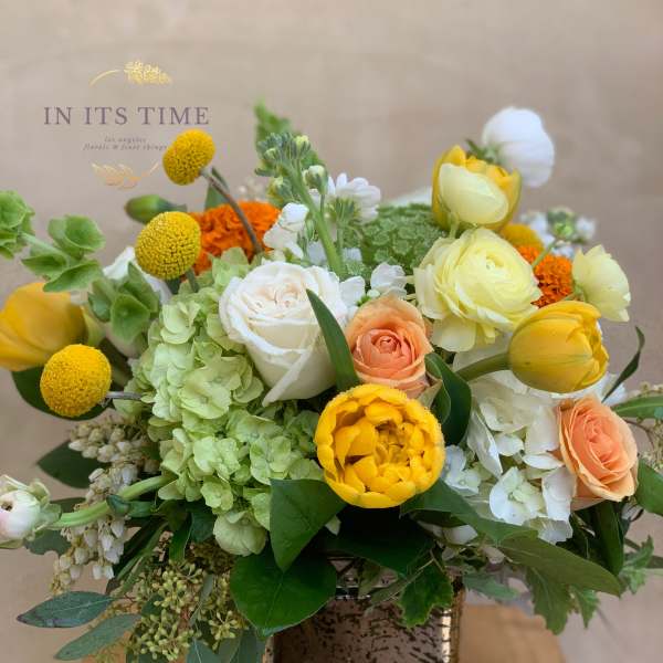 Mixed bouquet in a square ceramic vase with yellow, white, peach, and green blooms