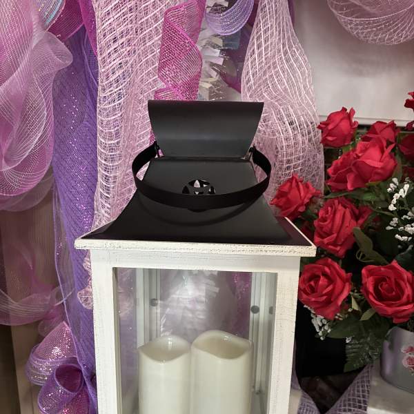 White lantern with two pillar candles beside red roses