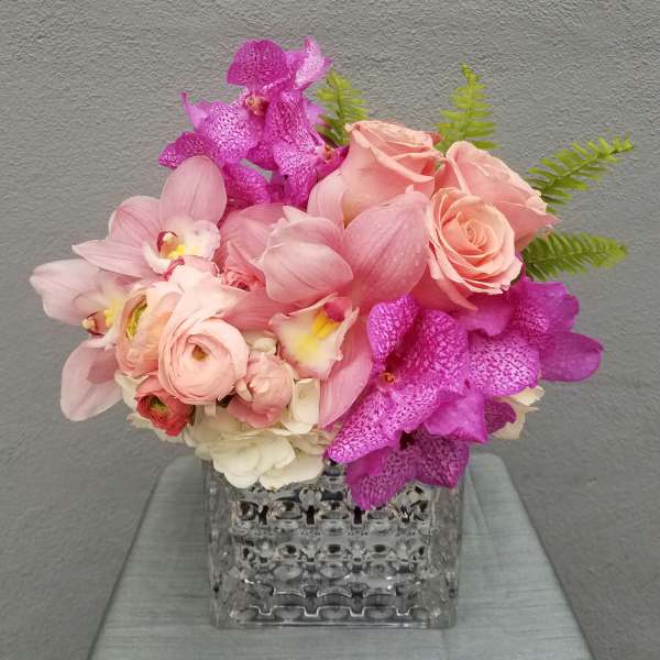 Pink roses and orchids arranged in a clear square vase