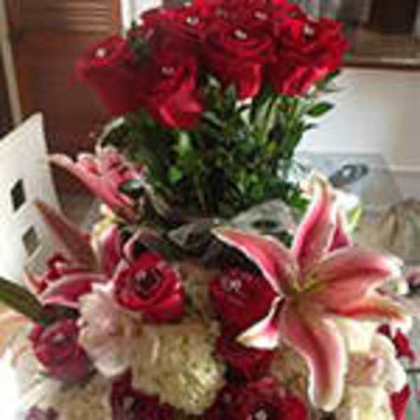 Tall arrangement of red roses with pink lilies and white blooms in a tiered design.