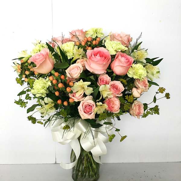 Pink roses and pale green carnations in a glass vase with a white ribbon