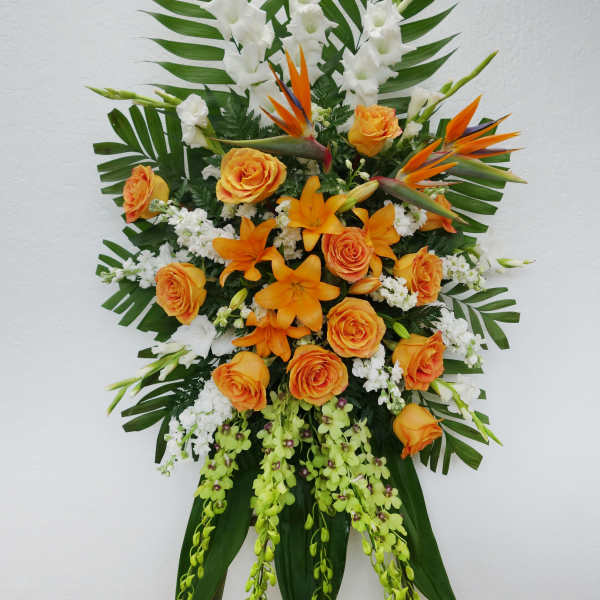 Tall standing floral spray with orange roses, white blooms, and tropical leaves