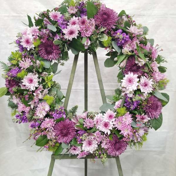 Large purple and pink floral wreath on a wooden easel against a light backdrop