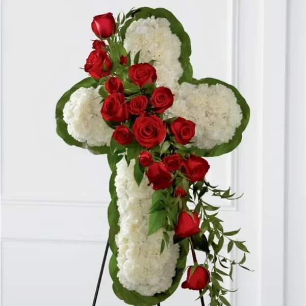 Standing floral cross of white blooms with cascading red roses on a metal easel.