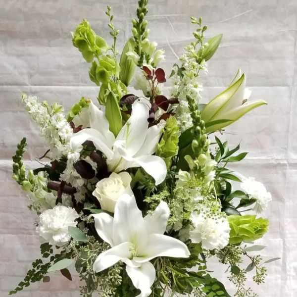 White lilies and green blooms in a clear glass vase