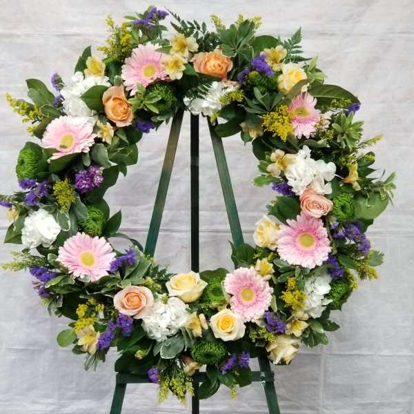 Floral wreath on a stand with pink, white, yellow, and purple flowers