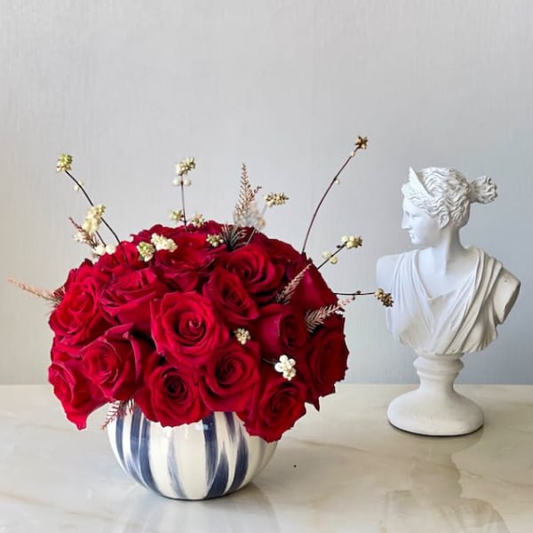 Red rose arrangement in a striped ceramic vase beside a white bust sculpture