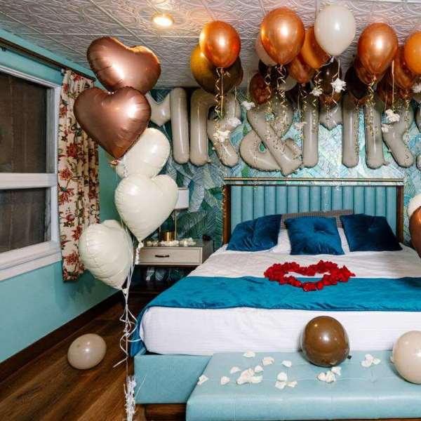 Bedroom decorated with heart-shaped balloons and rose petals on the bed