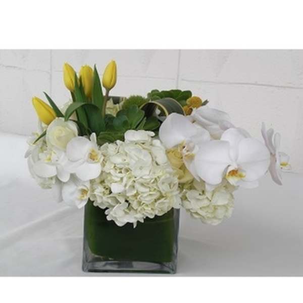 White orchids and hydrangeas with yellow tulips in a glass vase
