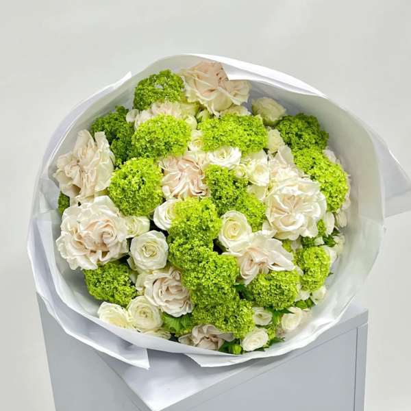 Bouquet of cream roses and bright green pom-pom flowers wrapped in white paper