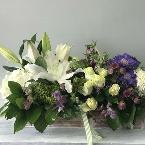 Low floral centerpiece with white lilies, cream roses, and purple blooms in a wooden box