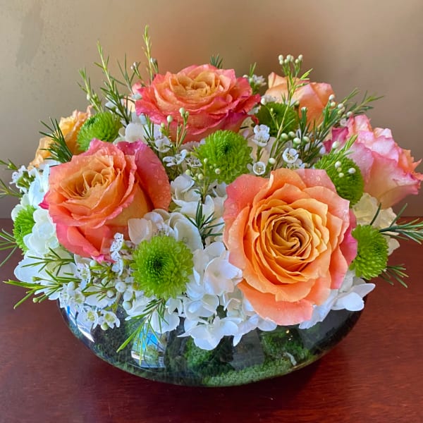 Peach and pink roses in a low glass bowl with white blooms and green accents