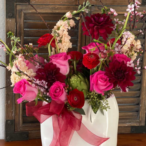 Pink and red floral arrangement in a white vase with a ribbon