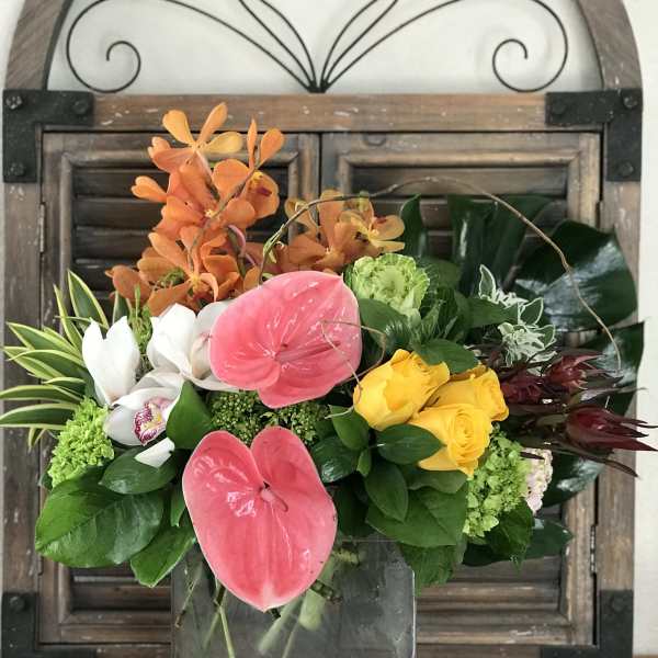 Mixed tropical bouquet in a glass vase with pink anthuriums and yellow roses