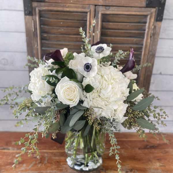 White bouquet with roses, hydrangeas, and dark calla lilies in a glass vase