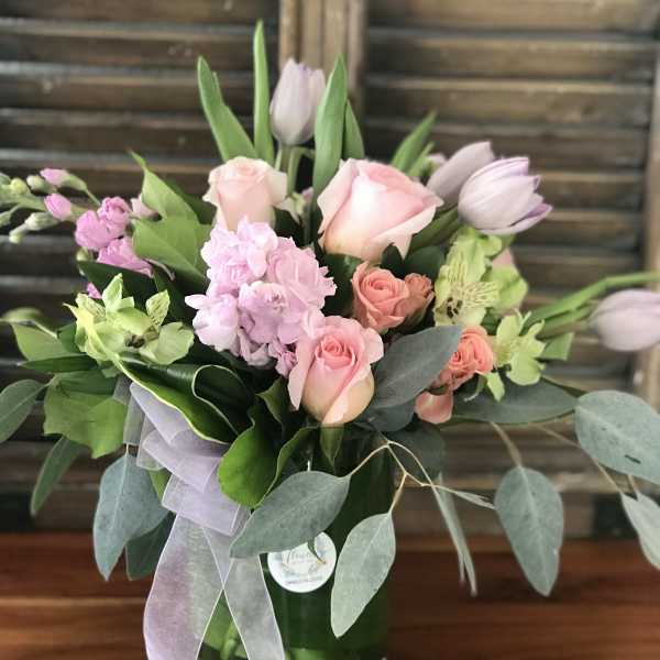 Pink roses and tulips arranged in a glass vase with ribbon