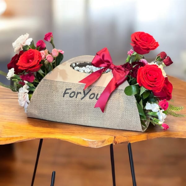 Flower arrangement in a burlap gift box with red roses and pink blooms