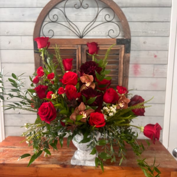 Red roses and orchids arranged in a white pedestal vase