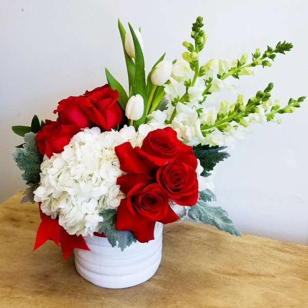 Red roses and white hydrangeas in a white vase with tulips and snapdragons