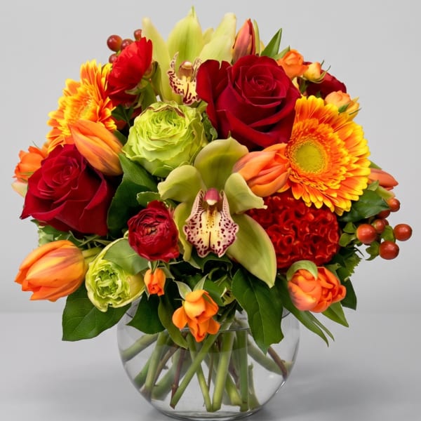 Mixed bouquet of red roses, orange gerberas, and lilies in a glass vase
