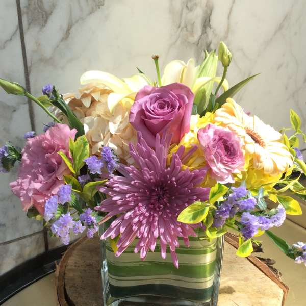 Mixed bouquet of pink, purple, yellow, and white flowers in a glass vase
