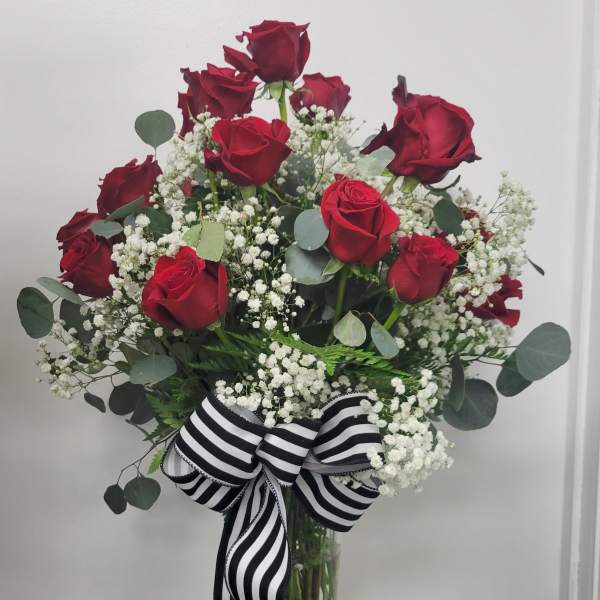 Red roses in a glass vase with white baby's breath and a striped ribbon