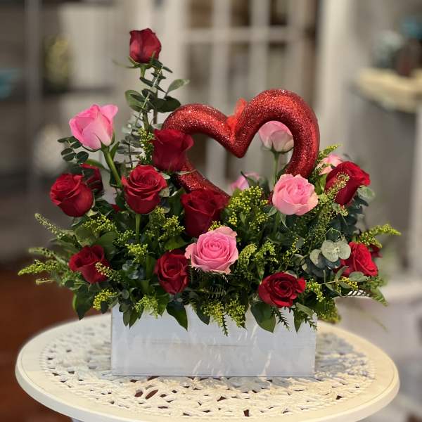Red and pink roses arranged in a white box with a glitter heart pick
