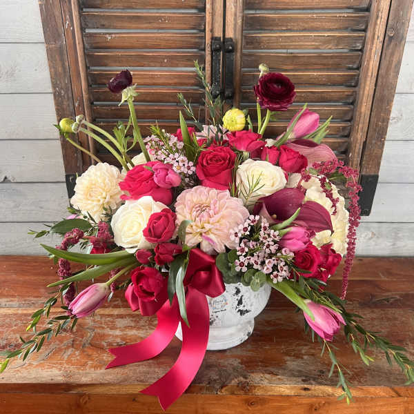 Mixed pink and white flower arrangement in a white vase with a pink ribbon