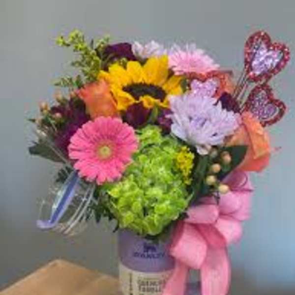 Colorful bouquet with a sunflower, gerbera daisies, and a pink ribbon in a purple vase