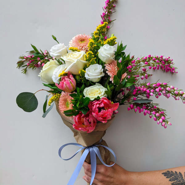 Hand-tied bouquet of white and pink flowers wrapped in brown paper with a blue ribbon