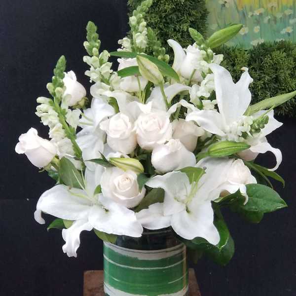White lilies and pale roses arranged in a green glass vase