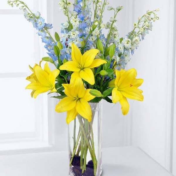 Yellow lilies and blue delphinium in a clear glass vase