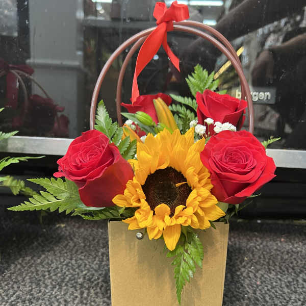 Red roses and a sunflower in a gold gift bag with a red ribbon