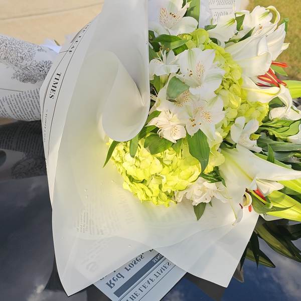 Bouquet of white lilies and green hydrangeas wrapped in white paper