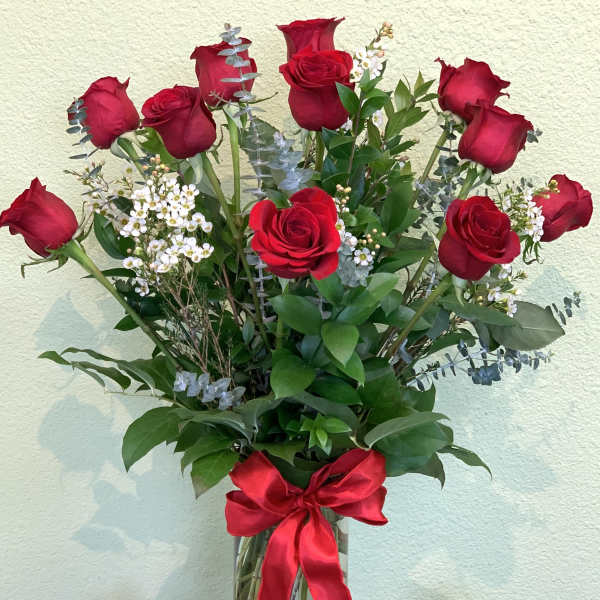 Tall bouquet of red roses in a glass vase with a red ribbon