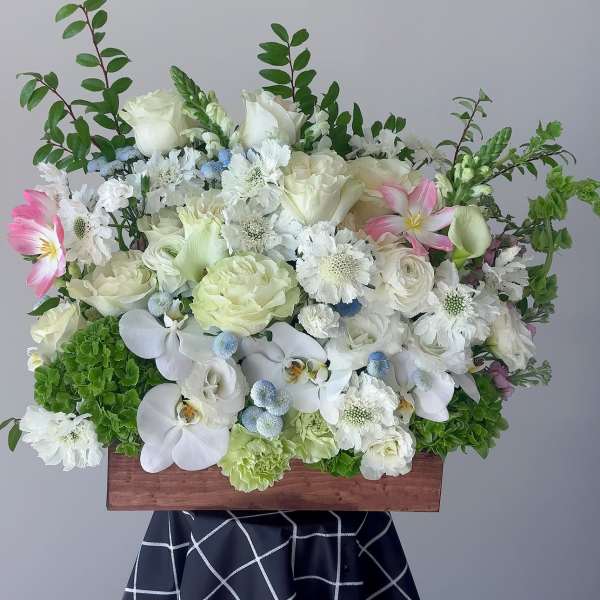 White floral arrangement with orchids and roses in a wooden box