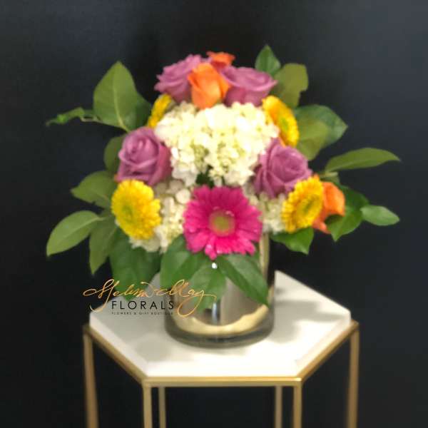 Colorful mixed flower arrangement in a glass vase on a small table
