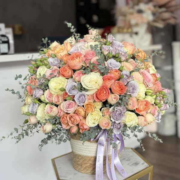 Large bouquet of pastel roses in a woven basket with a lavender ribbon