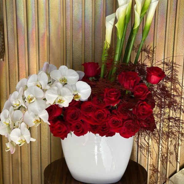 Red roses and white orchids in a white vase with tall calla lilies
