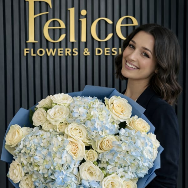 Large bouquet of cream roses and pale blue hydrangeas wrapped in blue paper
