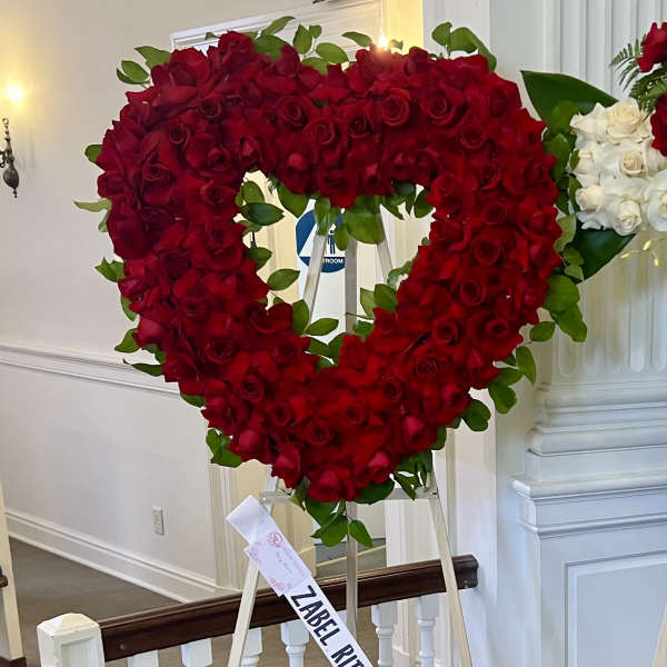 Heart-shaped red rose arrangement on an easel with a white rose cluster beside it