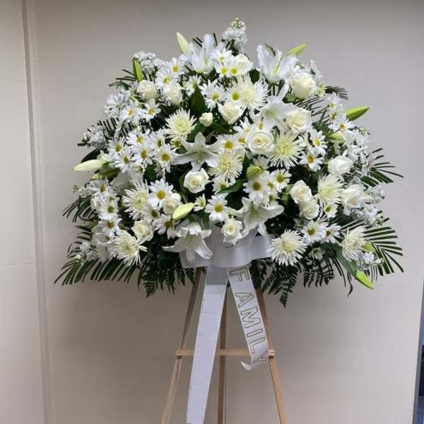 Large white funeral spray on an easel with a family ribbon