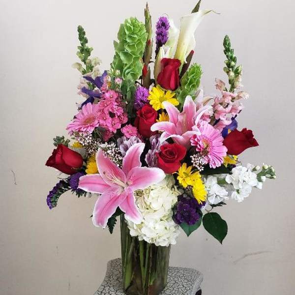 Tall mixed bouquet in a clear glass vase with pink lilies and red roses