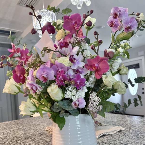 Tall arrangement of pink and purple orchids with white roses in a white ceramic vase