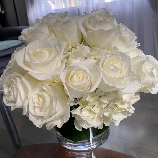 White roses and hydrangeas arranged in a clear glass vase