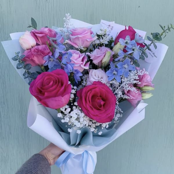 Bouquet of pink and blue roses with white filler flowers wrapped in white paper
