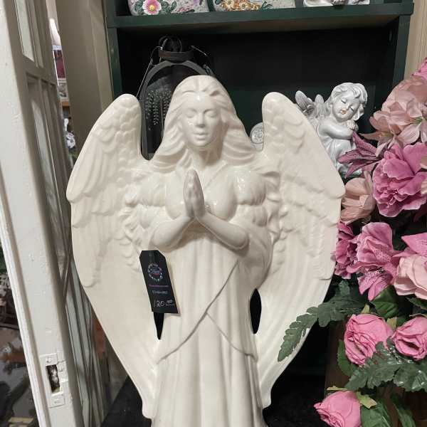 Ceramic praying angel statue beside pink artificial flowers