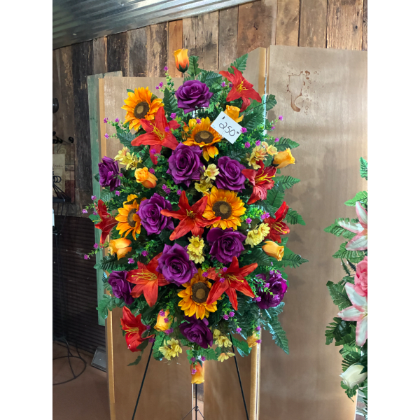 Tall floral standing spray with purple roses, red lilies, and sunflowers